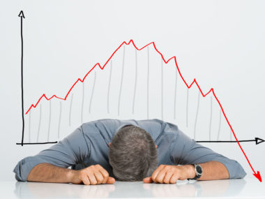 depressed businessman leaning his head below a bad stock market chart