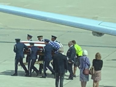 coffin with american flag being carried off tarmac